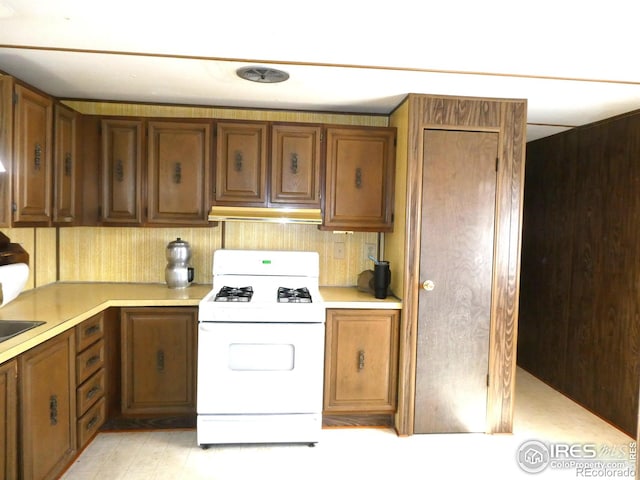 317 N Ord St, Grover, CO 80729 - kitchen featuring under cabinet range hood, light countertops, brown cabinetry, and white gas range oven