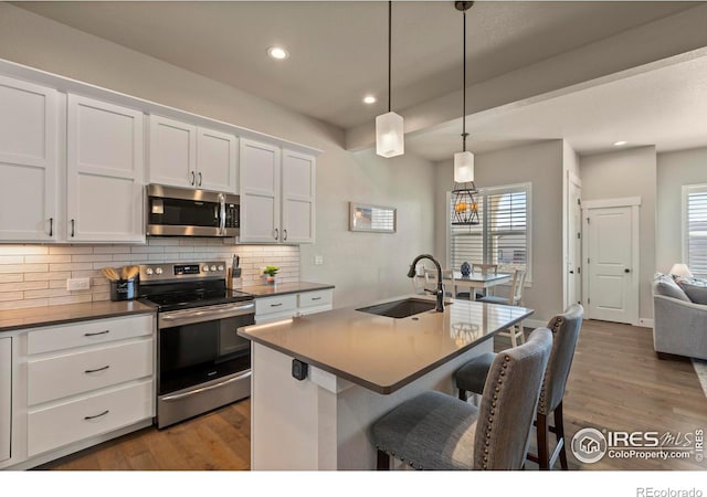 1708 W 50th St, Loveland, CO 80538 - kitchen with a kitchen breakfast bar, decorative backsplash, stainless steel appliances, a sink, and wood finished floors