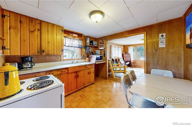 kitchen featuring white appliances, healthy amount of natural light, wooden walls, brown cabinets, and light countertops