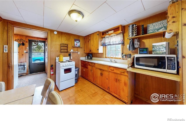 kitchen with white appliances, plenty of natural light, wood walls, light countertops, and a sink