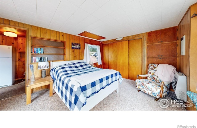 bedroom with freestanding refrigerator, carpet, and wooden walls