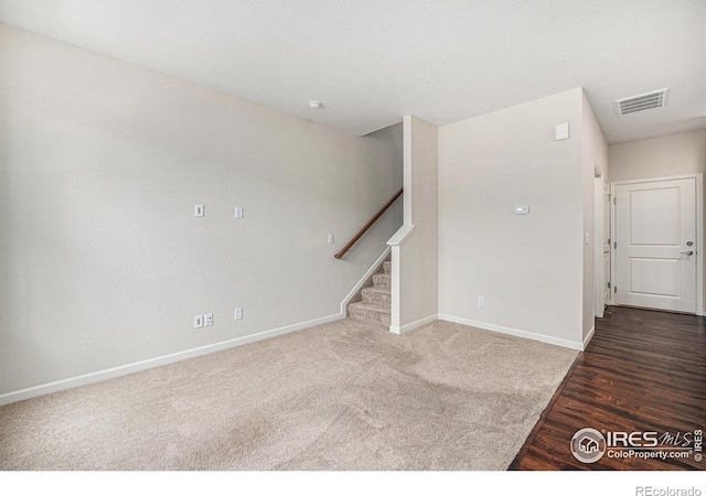 carpeted spare room featuring visible vents, baseboards, wood finished floors, and stairs