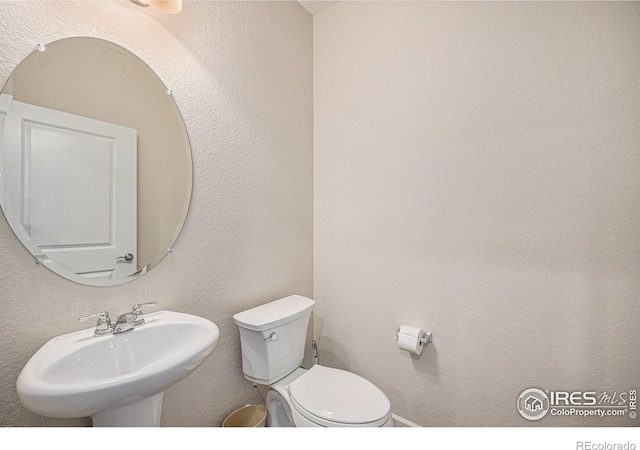 bathroom with a sink, toilet, and a textured wall