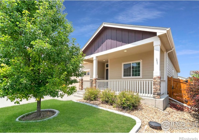 craftsman-style home with a porch, board and batten siding, stone siding, and a front lawn