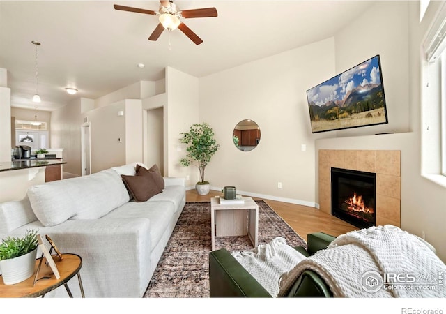 living room with ceiling fan, baseboards, wood finished floors, and a fireplace