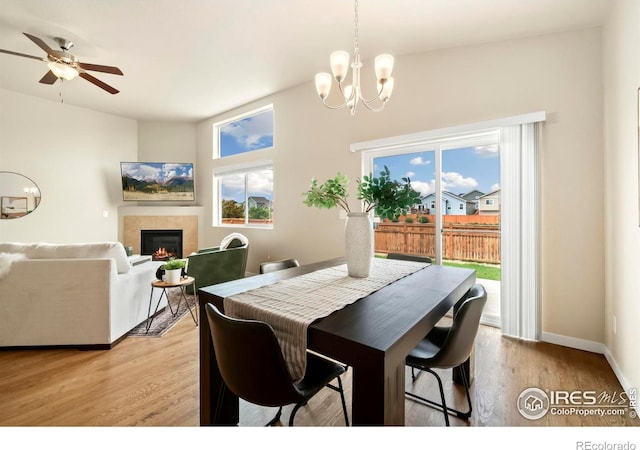 dining area with a fireplace, light wood finished floors, baseboards, and ceiling fan with notable chandelier