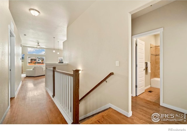 corridor with light wood-type flooring, an upstairs landing, and baseboards