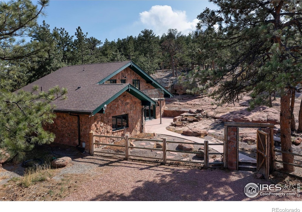1740 Spring Gulch Dr, Lyons, CO 80540 - rustic home featuring roof with shingles, a fenced front yard, stone siding, and a gate