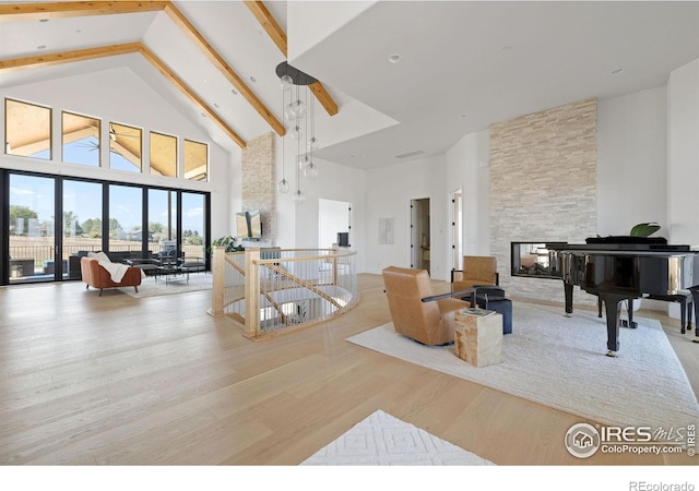 living area with high vaulted ceiling, a stone fireplace, beam ceiling, and wood finished floors