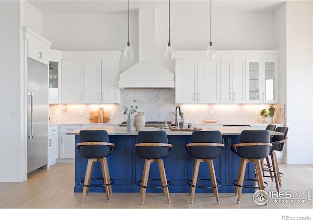 kitchen featuring glass insert cabinets, stainless steel built in refrigerator, white cabinets, custom exhaust hood, and light countertops