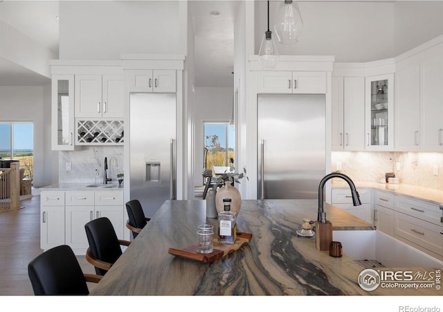 kitchen with a sink, built in refrigerator, and white cabinets