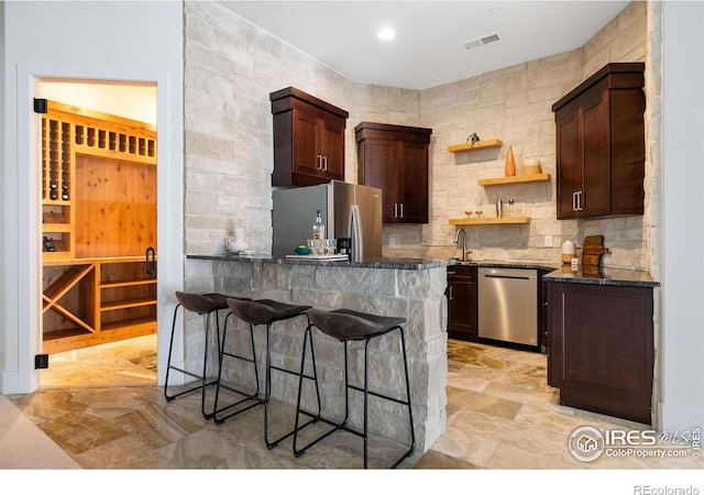kitchen with a kitchen bar, a peninsula, open shelves, dark stone countertops, and stainless steel appliances
