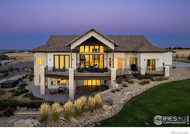 back of property at dusk featuring a patio, stucco siding, a deck, and a lawn
