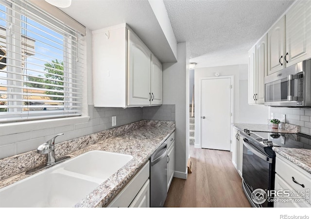 1616 Longbow Ct, Lafayette, CO 80026 - kitchen featuring appliances with stainless steel finishes, wood finished floors, tasteful backsplash, white cabinets, and a textured ceiling