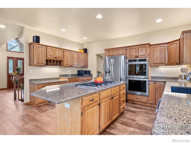 kitchen with a center island, a sink, light stone counters, stainless steel appliances, and light wood-style flooring