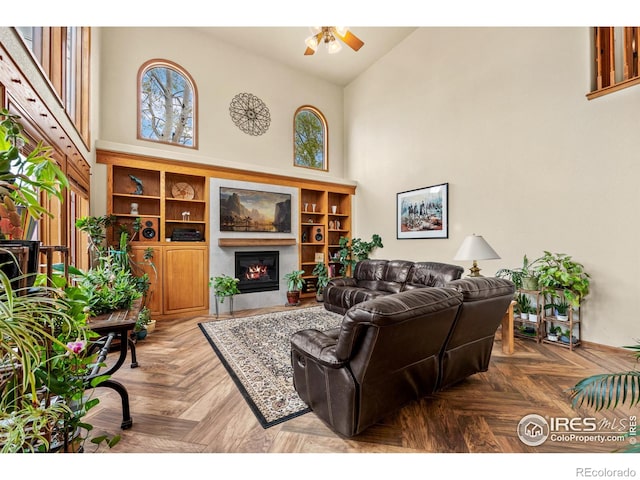 living area with a glass covered fireplace, ceiling fan, a healthy amount of sunlight, and high vaulted ceiling