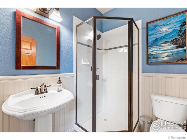 bathroom featuring a shower stall, wainscoting, a sink, toilet, and a textured wall