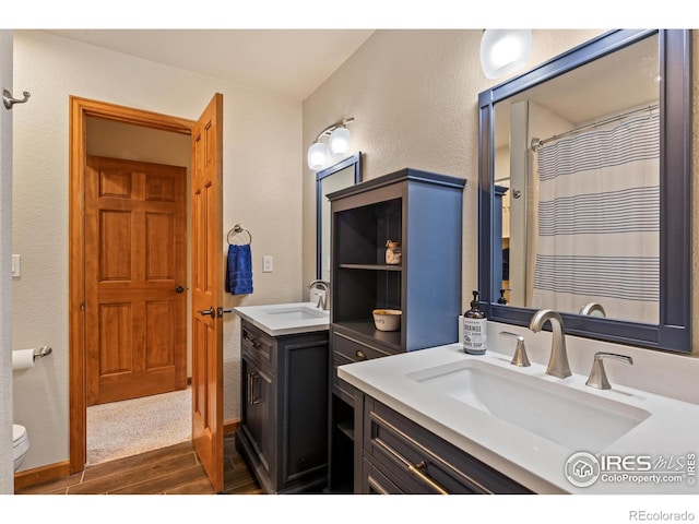 bathroom featuring a sink, a textured wall, wood finished floors, and two vanities