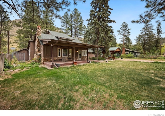 198 Poudre River Rd, Bellvue, CO 80512 - back of house featuring fence, stone siding, an outbuilding, a chimney, and a yard