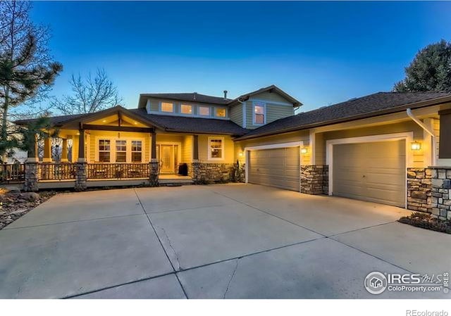view of front of property with an attached garage, a porch, driveway, and stone siding