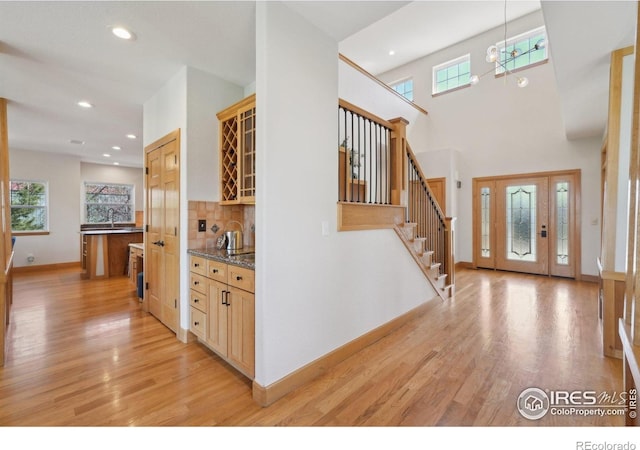 foyer entrance with light wood finished floors, baseboards, recessed lighting, stairs, and indoor wet bar