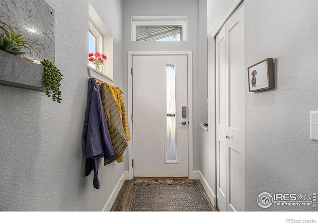 doorway with wood finished floors, a textured wall, and baseboards