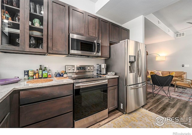 kitchen featuring glass insert cabinets, dark brown cabinets, dark wood-type flooring, visible vents, and stainless steel appliances