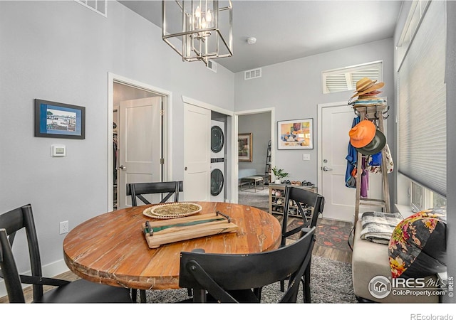 dining space with a notable chandelier, visible vents, wood finished floors, and stacked washer and clothes dryer