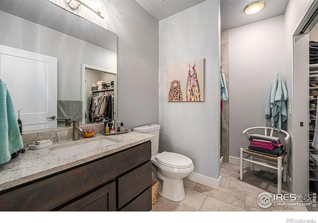 full bath featuring vanity, toilet, a walk in closet, walk in shower, and baseboards