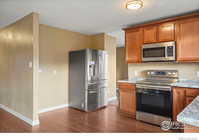 1458 Friendship Ln W, Colorado Springs, CO 80904 - kitchen with baseboards, appliances with stainless steel finishes, brown cabinetry, light stone countertops, and dark wood-type flooring
