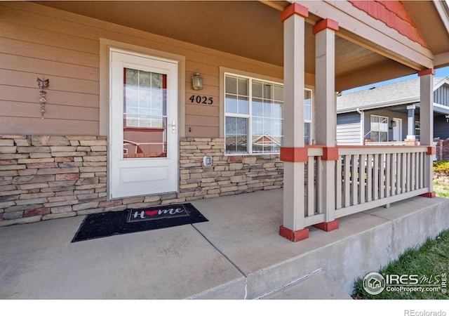 view of exterior entry featuring stone siding and covered porch