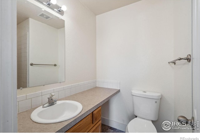 bathroom with toilet, vanity, backsplash, and visible vents