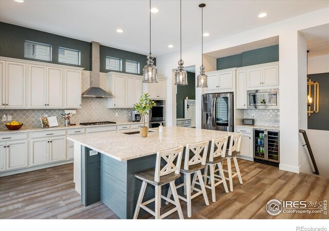 16392 Spanish Peak Way, Broomfield, CO 80023 - kitchen with wine cooler, stainless steel appliances, wall chimney range hood, tasteful backsplash, and light wood finished floors