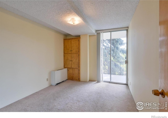 empty room featuring carpet floors, a textured ceiling, radiator, and floor to ceiling windows