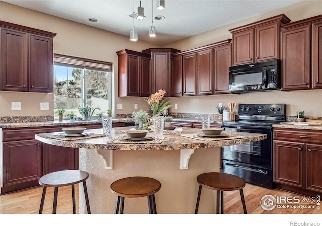 5036 Ridgewood Dr, Johnstown, CO 80534 - kitchen featuring light wood-type flooring, black appliances, a kitchen island, a breakfast bar, and decorative light fixtures