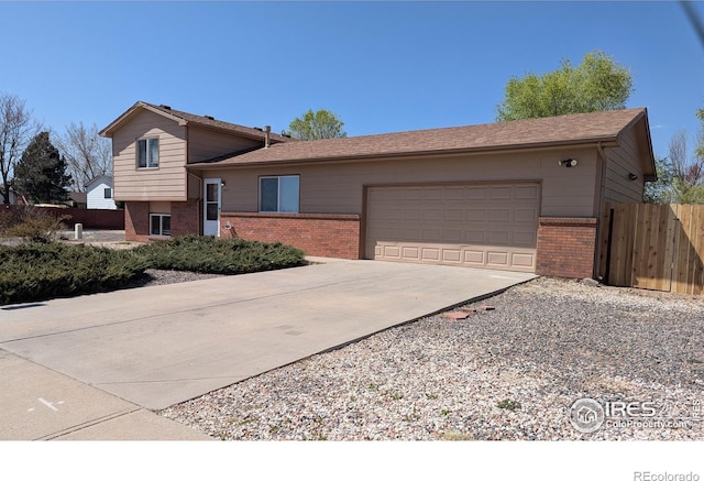 tri-level home with an attached garage, driveway, fence, and brick siding