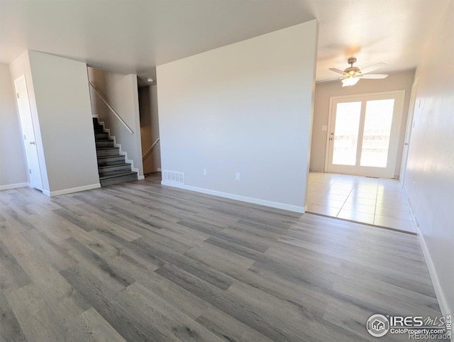 unfurnished living room featuring a ceiling fan, visible vents, wood finished floors, stairs, and baseboards