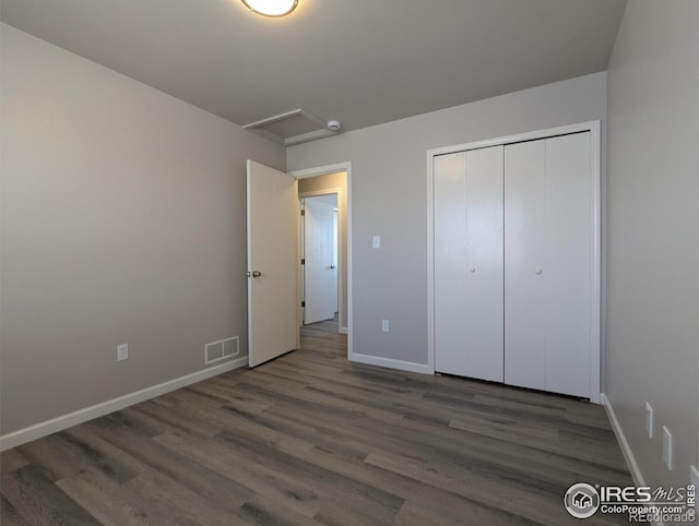 unfurnished bedroom with visible vents, baseboards, a closet, attic access, and wood finished floors