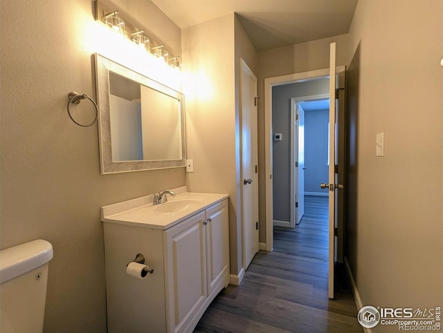 half bath with toilet, vanity, wood finished floors, and baseboards