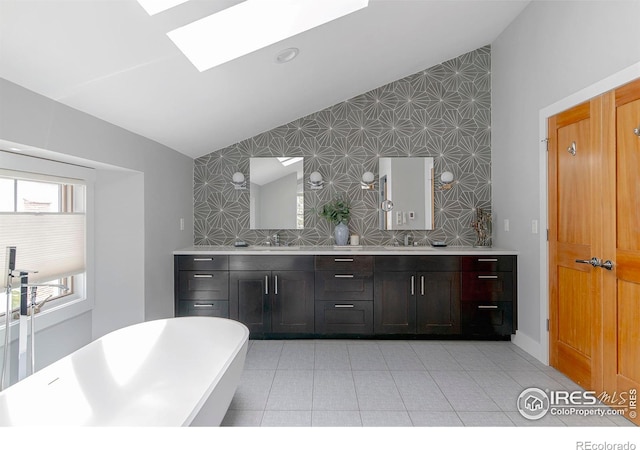full bathroom featuring double vanity, lofted ceiling with skylight, a sink, and an accent wall