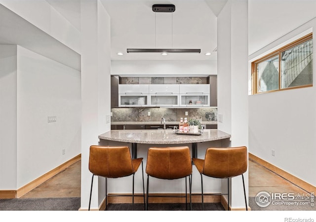 kitchen featuring decorative backsplash, a kitchen bar, light stone counters, baseboards, and white cabinetry