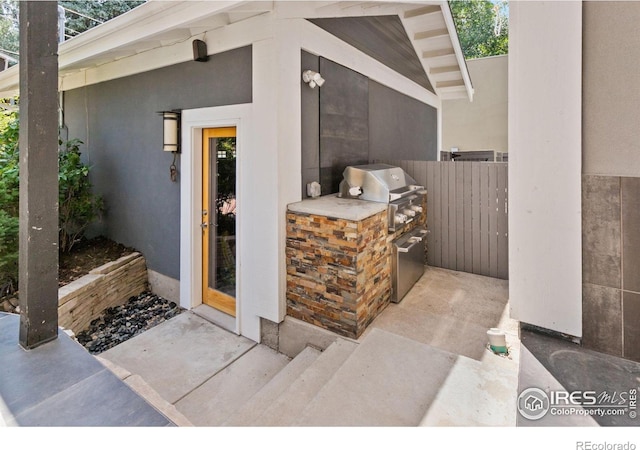 view of exterior entry with exterior kitchen, fence, and stucco siding