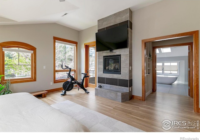 bedroom featuring baseboards, vaulted ceiling, a tiled fireplace, and wood finished floors