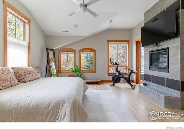 bedroom featuring visible vents, a fireplace, vaulted ceiling, wood finished floors, and baseboards