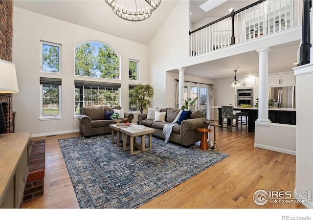 4939 Yoke Ct, Loveland, CO 80537 - living area featuring decorative columns, a brick fireplace, a towering ceiling, light wood-style flooring, and a chandelier