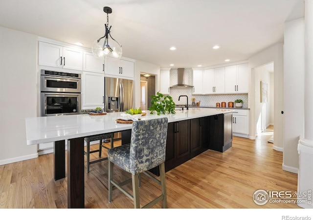 4939 Yoke Ct, Loveland, CO 80537 - kitchen with wall chimney range hood, stainless steel appliances, white cabinets, decorative backsplash, and light wood-type flooring