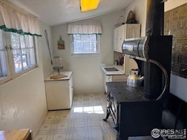 kitchen with a healthy amount of sunlight, a wood stove, lofted ceiling, and light floors