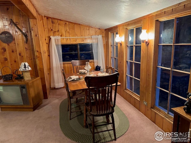 carpeted dining space featuring a textured ceiling, wooden walls, and vaulted ceiling