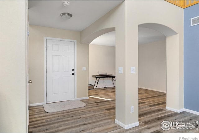entrance foyer with arched walkways, visible vents, baseboards, and wood finished floors