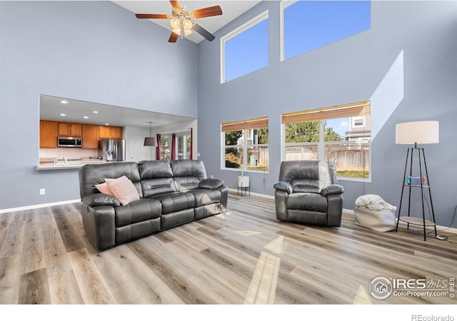 living area with light wood finished floors, a healthy amount of sunlight, ceiling fan, and baseboards
